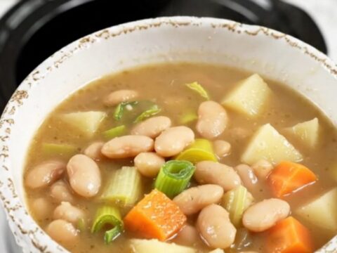 A rustic bowl of white bean and leek soup with visible chunks of potato and carrots.