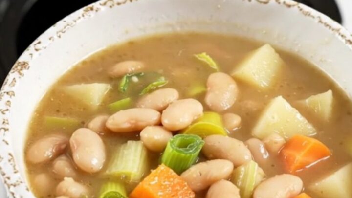 A rustic bowl of white bean and leek soup with visible chunks of potato and carrots.