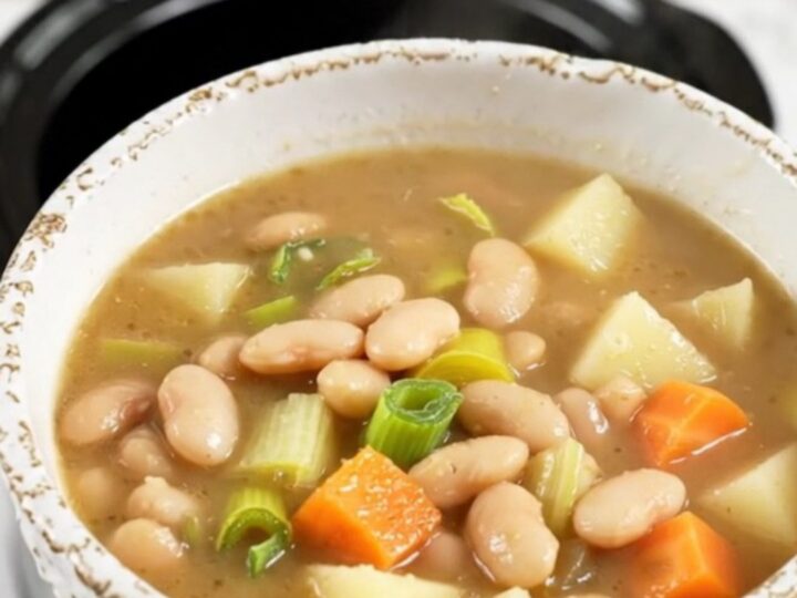 A rustic bowl of white bean and leek soup with visible chunks of potato and carrots.