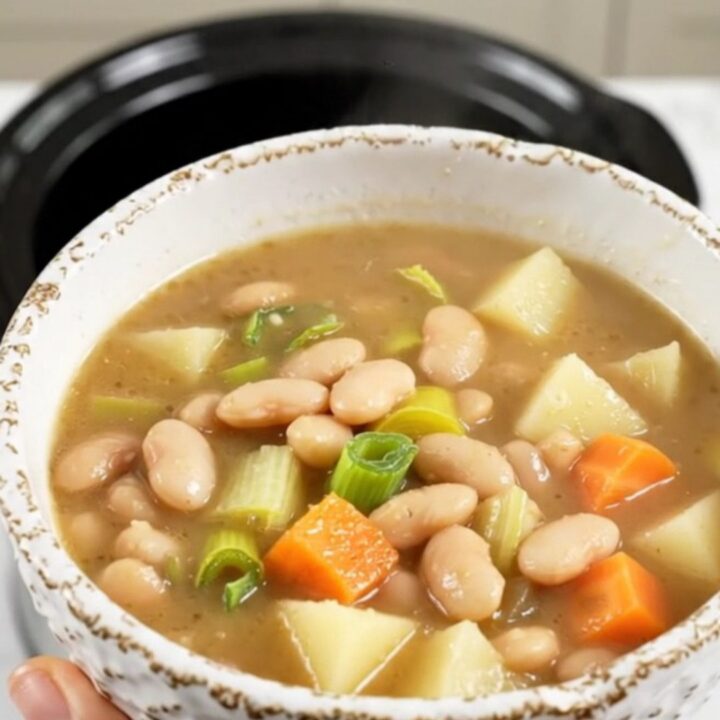A rustic bowl of white bean and leek soup with visible chunks of potato and carrots.