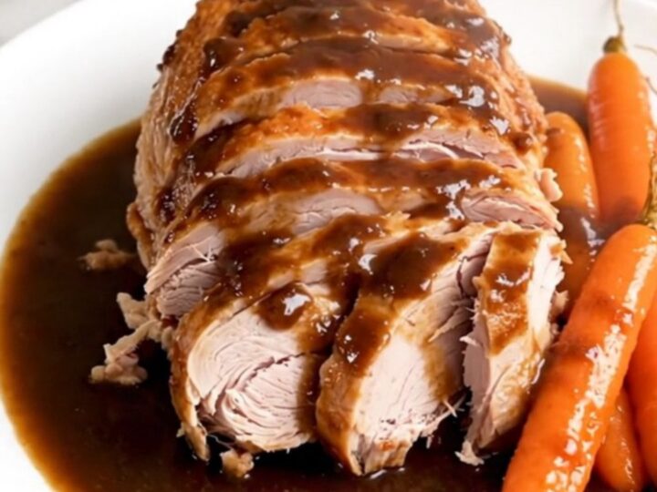 A sliced turkey roast with carrots and a glossy reduction, presented on a white plate.