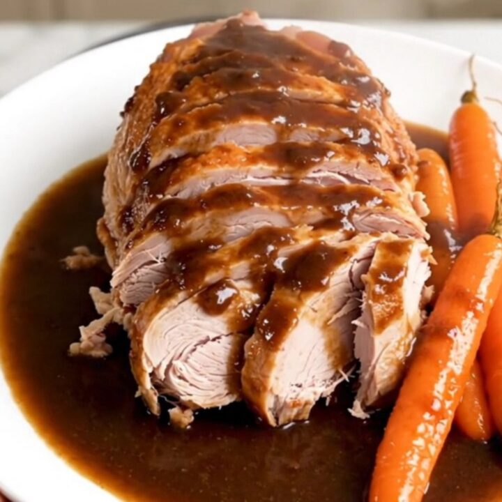 A sliced turkey roast with carrots and a glossy reduction, presented on a white plate.