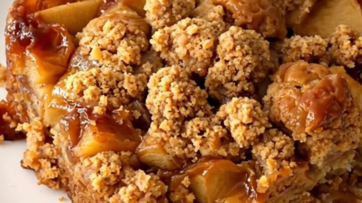A close-up of a warm apple speculoos crumble served on a white plate with visible steam.