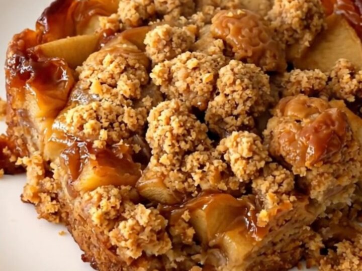 A close-up of a warm apple speculoos crumble served on a white plate with visible steam.