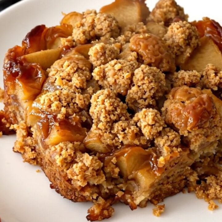 A close-up of a warm apple speculoos crumble served on a white plate with visible steam.