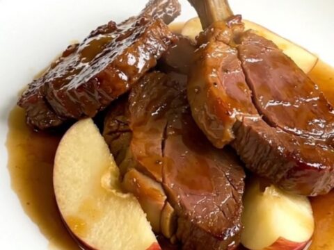 A top-down view of raw veal tendrons, apple wedges, and sliced onions in a slow cooker, ready to be cooked.