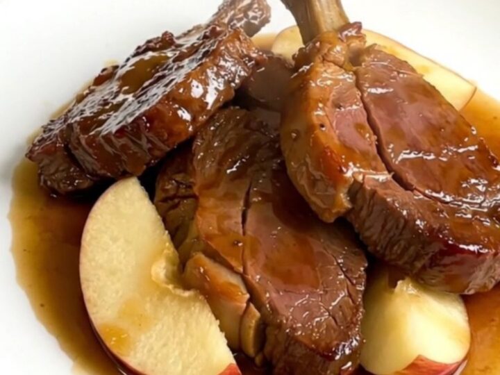 A top-down view of raw veal tendrons, apple wedges, and sliced onions in a slow cooker, ready to be cooked.