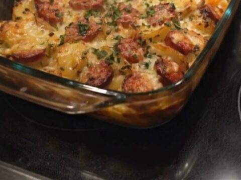 A bubbling, golden-brown cheesy sausage potato bake in a glass dish, garnished with fresh herbs.