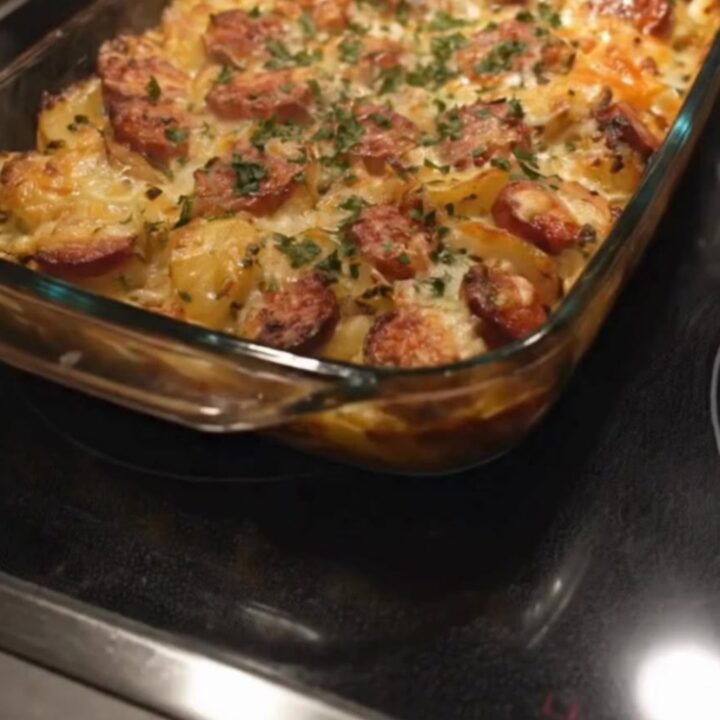 A bubbling, golden-brown cheesy sausage potato bake in a glass dish, garnished with fresh herbs.