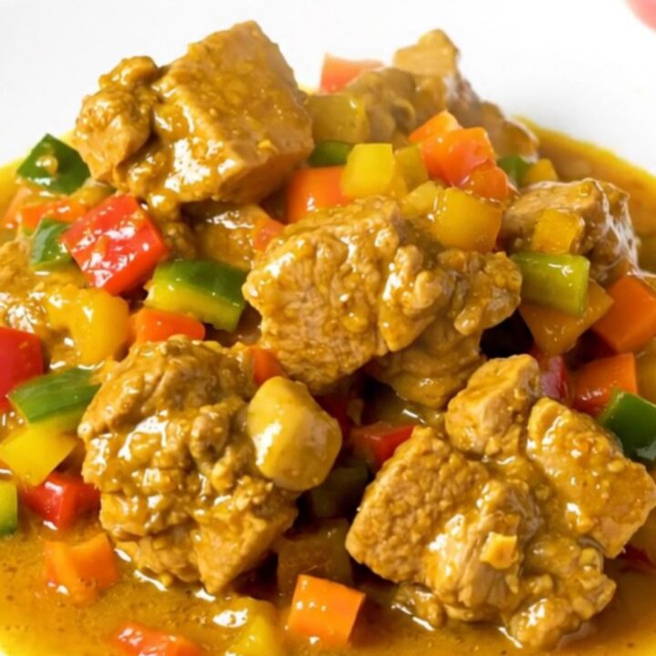 A close-up of a glossy, steaming pork colombo dish served on a white plate.