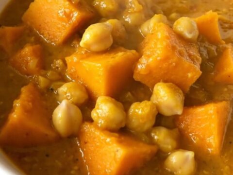 A steaming, golden bowl of butternut squash and chickpea curry topped with fresh herbs.