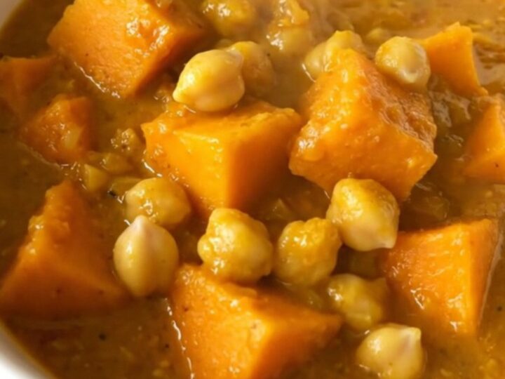 A steaming, golden bowl of butternut squash and chickpea curry topped with fresh herbs.