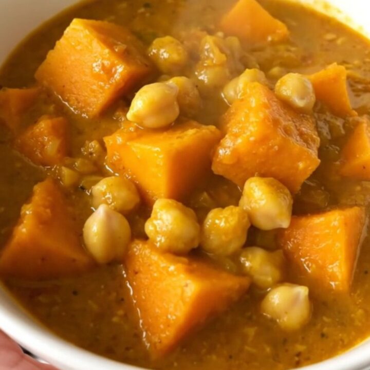 A steaming, golden bowl of butternut squash and chickpea curry topped with fresh herbs.