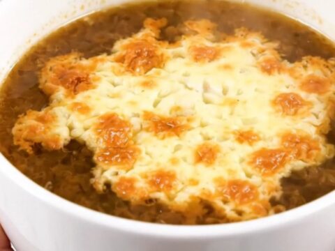 A steaming bowl of French onion soup with a golden, bubbly layer of melted Comté cheese on top.
