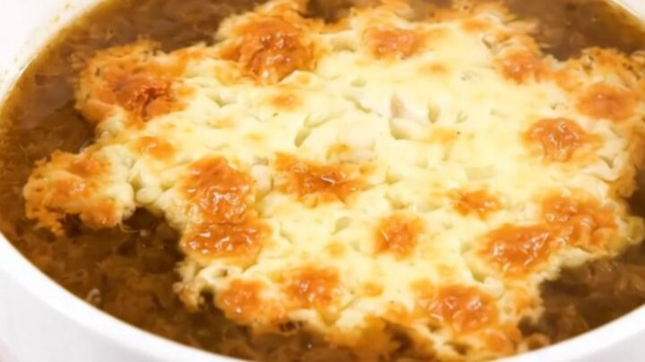 A steaming bowl of French onion soup with a golden, bubbly layer of melted Comté cheese on top.
