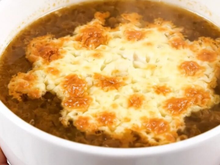 A steaming bowl of French onion soup with a golden, bubbly layer of melted Comté cheese on top.