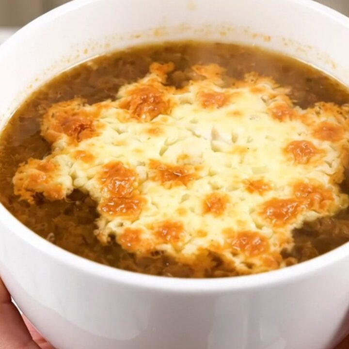 A steaming bowl of French onion soup with a golden, bubbly layer of melted Comté cheese on top.
