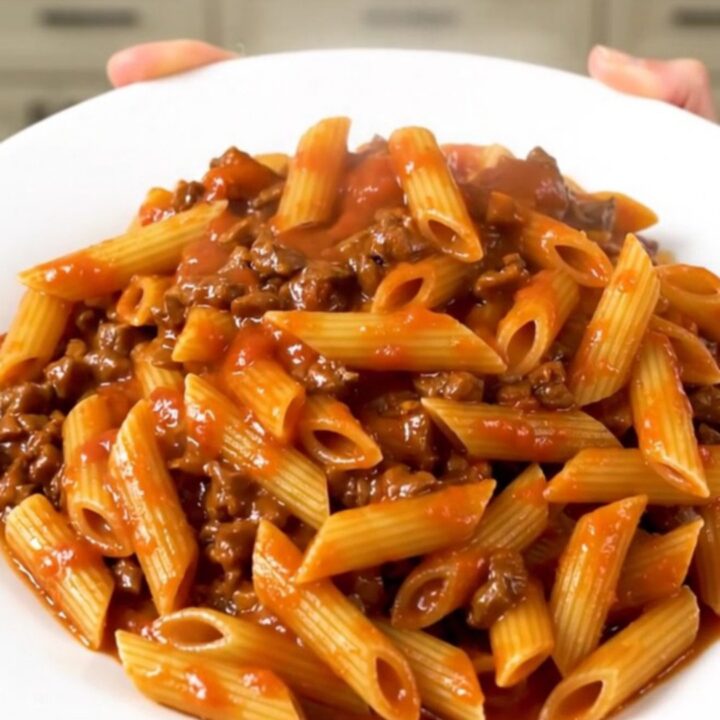 A top-down view of a slow cooker filled with raw ground beef, dry penne pasta, and tomato sauce, ready to cook.