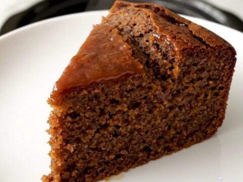 A warm, sliced gingerbread cake served on a white plate with a soft, blurred kitchen background.