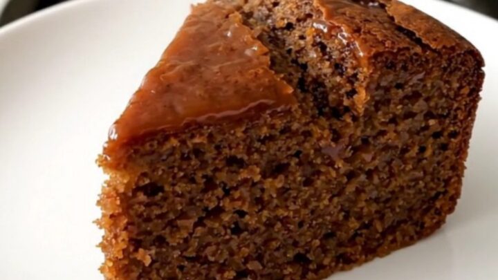 A warm, sliced gingerbread cake served on a white plate with a soft, blurred kitchen background.
