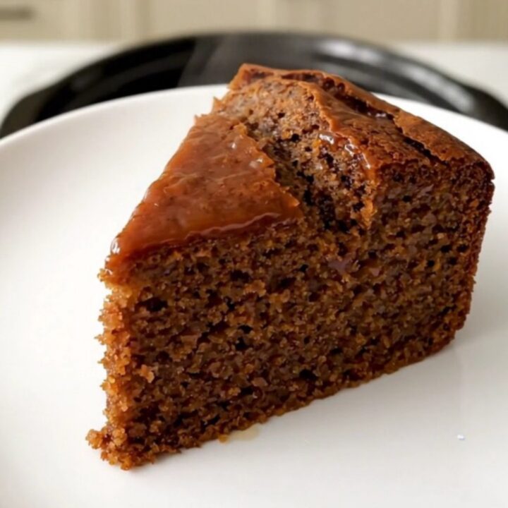 A warm, sliced gingerbread cake served on a white plate with a soft, blurred kitchen background.
