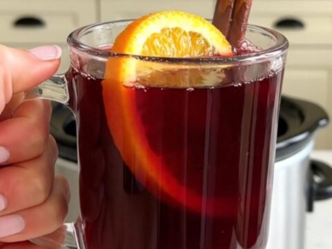 Un mug en verre rempli de vin chaud fumant garni d'une tranche d'orange et d'un bâton de cannelle.