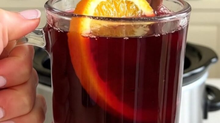 Un mug en verre rempli de vin chaud fumant garni d'une tranche d'orange et d'un bâton de cannelle.
