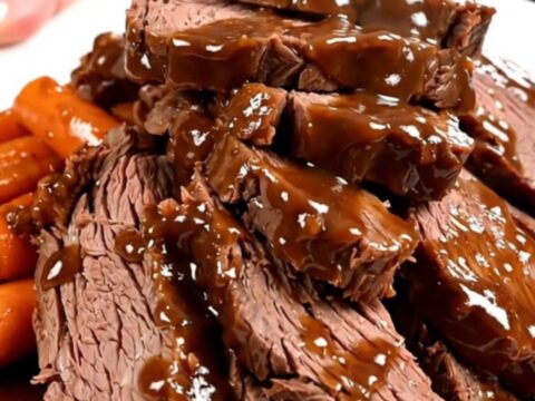 A close-up of tender, sliced beef chuck roast covered in a rich, glossy dark sauce with glazed carrots on a white plate.