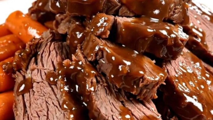 A close-up of tender, sliced beef chuck roast covered in a rich, glossy dark sauce with glazed carrots on a white plate.