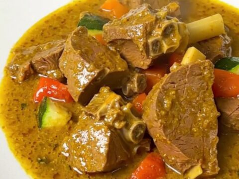 A steaming bowl of creamy coconut curry veal with sliced zucchini and onions in a rich, glossy sauce.