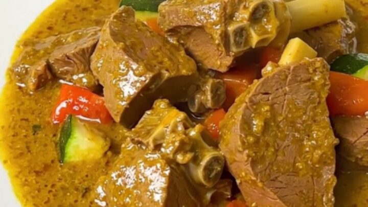 A steaming bowl of creamy coconut curry veal with sliced zucchini and onions in a rich, glossy sauce.
