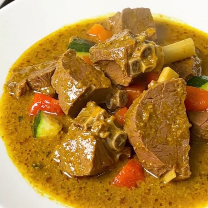 A steaming bowl of creamy coconut curry veal with sliced zucchini and onions in a rich, glossy sauce.