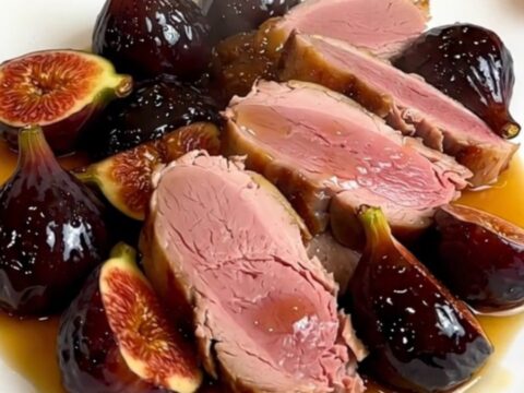 A slow cooker filled with duck breasts, halved figs, and shallots simmering in a rich honey-balsamic sauce.