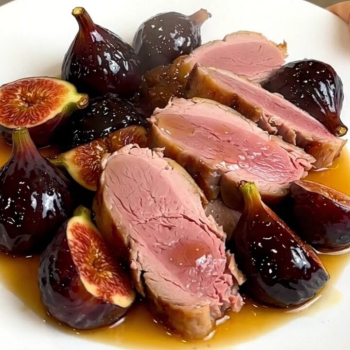 A slow cooker filled with duck breasts, halved figs, and shallots simmering in a rich honey-balsamic sauce.