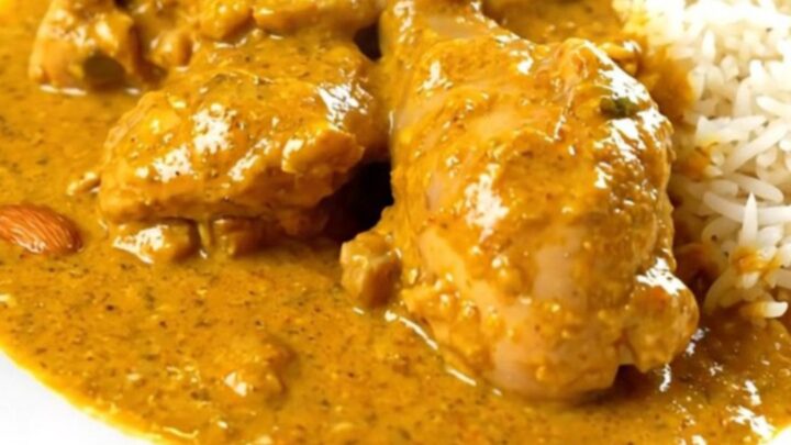 A steaming, glossy bowl of creamy chicken korma served with a side of fluffy white rice on a clean white plate.