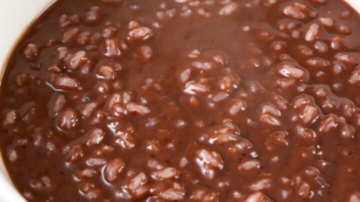 A black slow cooker filled with creamy dark chocolate rice pudding on a white speckled quartz countertop.