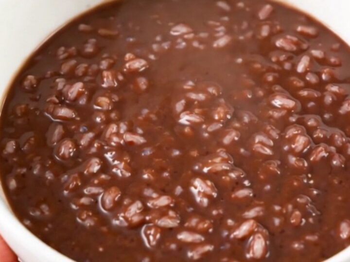 A black slow cooker filled with creamy dark chocolate rice pudding on a white speckled quartz countertop.