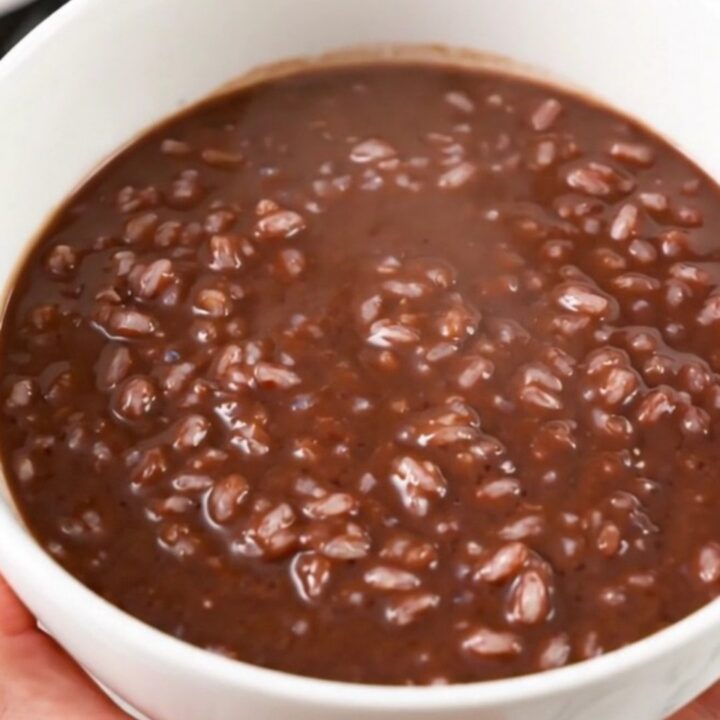A black slow cooker filled with creamy dark chocolate rice pudding on a white speckled quartz countertop.