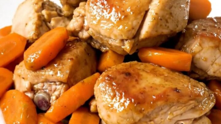 A slow cooker filled with chicken thighs, sliced carrots, and onions in a flavorful broth.