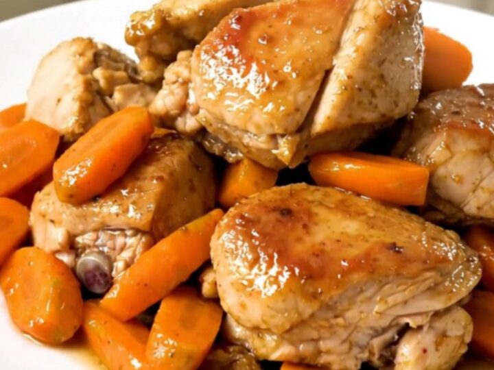 A slow cooker filled with chicken thighs, sliced carrots, and onions in a flavorful broth.