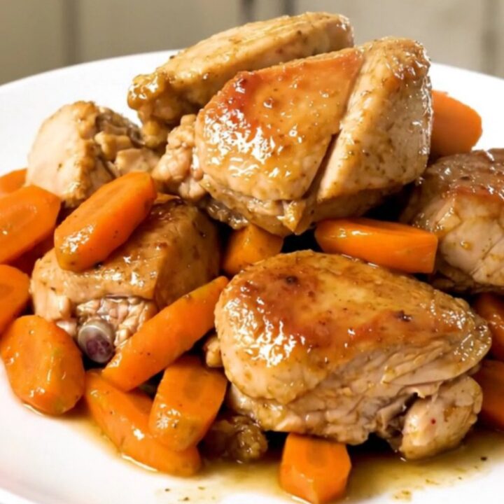 A slow cooker filled with chicken thighs, sliced carrots, and onions in a flavorful broth.