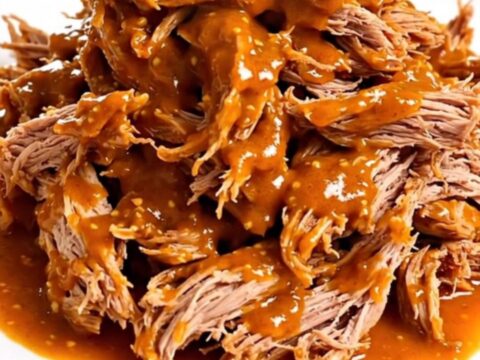 A close-up of tender, shredded pork shoulder coated in a glossy, spicy red mustard-tomato sauce on a white plate.