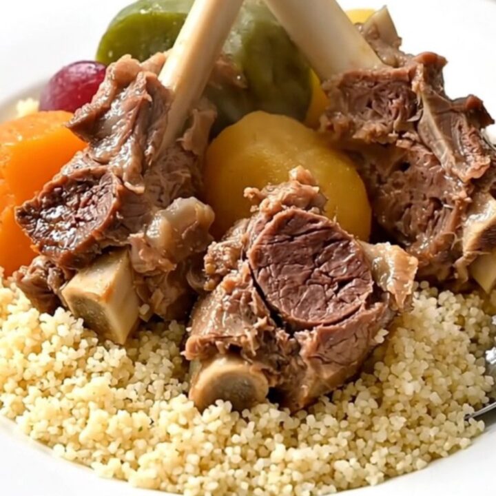 A white bowl filled with tender pieces of lamb and root vegetables served over fluffy semolina.