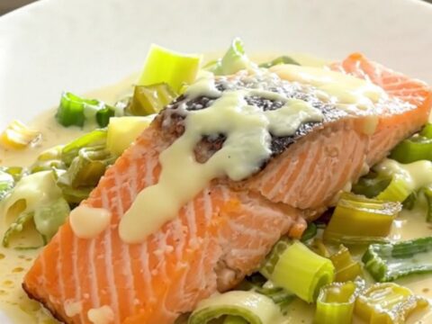 A top-down view of salmon fillets, sliced leeks, and dollops of crème fraîche in a black slow cooker insert.