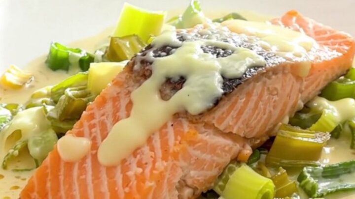 A top-down view of salmon fillets, sliced leeks, and dollops of crème fraîche in a black slow cooker insert.