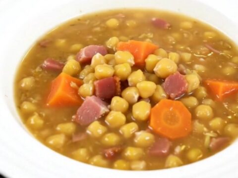 A steaming bowl of split pea and smoked bacon soup on a wooden table.