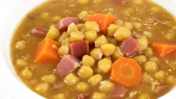 A steaming bowl of split pea and smoked bacon soup on a wooden table.