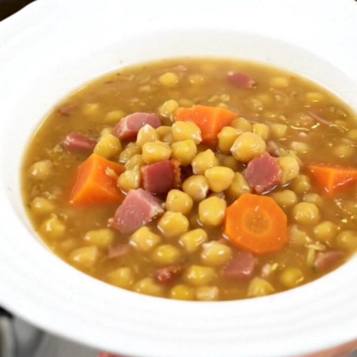 A steaming bowl of split pea and smoked bacon soup on a wooden table.