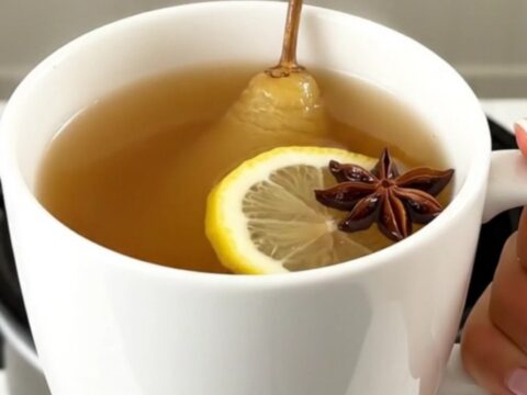 A steaming mug of spiced pear juice with a cinnamon stick and star anise, set against a blurred kitchen background.