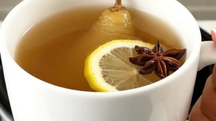 A steaming mug of spiced pear juice with a cinnamon stick and star anise, set against a blurred kitchen background.